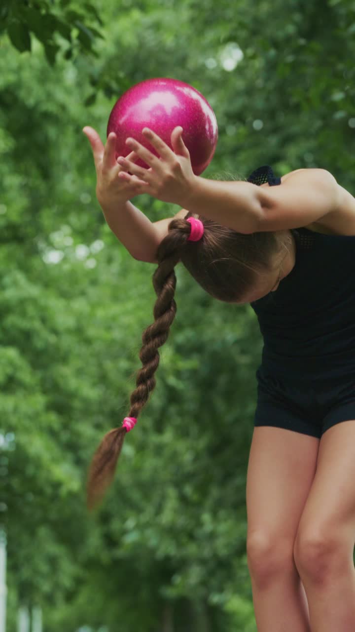 Young Girl Practicing Precision Skills with a Pink Ball in a Lush Green Outdoor Setting, Demonstrating Focus and Determination in Her Activity