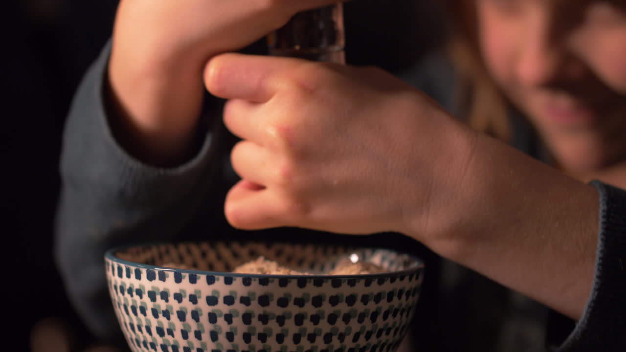 Close up on little girl's hands grinding vanilla into a bowl with baking mix