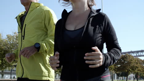 couple of happy mature runners jogging down street