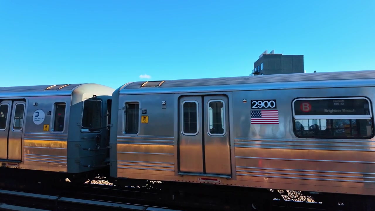 New York City metrotog under klar blå himmel. En rustfri stålvogn fylder billedet ved siden af forhøjede spor i dagslys.