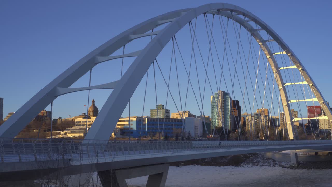 에드먼튼 시내의 배경 스카이라인과 함께 금속 스트랩에 빛을 반사하는 동안 얼어붙은 노스 서스캐처원 강 위의 트와일라잇 포스트 모던 미래 월터 데일 다리 일몰 겨울 오후