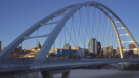 twilight post modern futuristic walter dale bridge sunset winter afternoon over north saskatchewan river frozen over reflecting light on metal straps with the background skyline of downtown edmonton