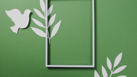 close up of white dove with frame and leaves and copy space on green background