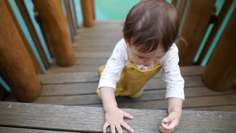 cute asian-ukrainian girl toddler learning to climb stairs on a wooden playground set - slow motion