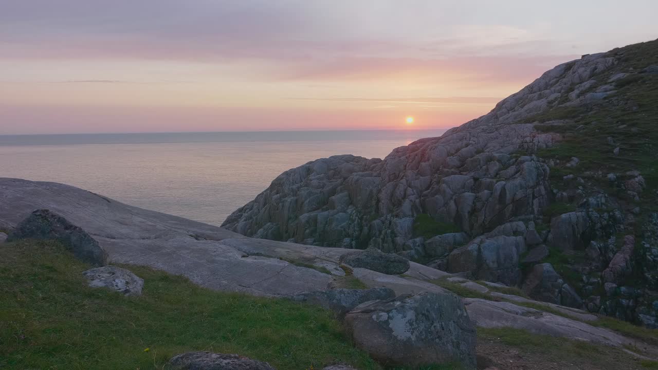 Sheigra sunset, Scotland. Camera pans left across rocky cliffs and green grass with the Atlantic horizon glowing under pastel skies