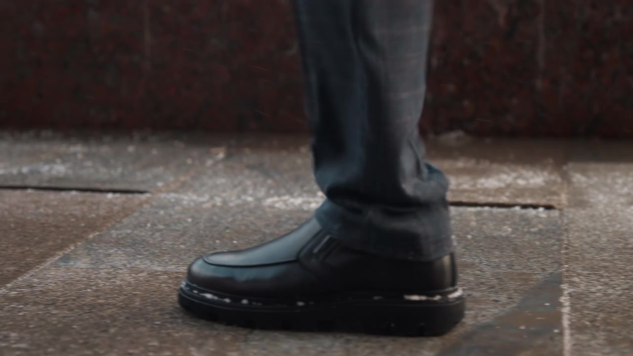Close up of man black leather shoes walking on wet stone pavement capturing movement and texture details. scene focuses solely on foot motion against urban outdoor background with no other