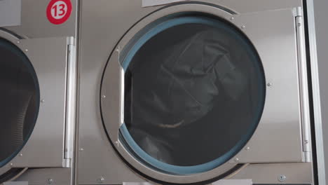 Front load industrial washing machine in operation with fabric rolling inside drum behind round glass door, stainless housing in laundromat, cycle running, close up spin and motion, cleaning process