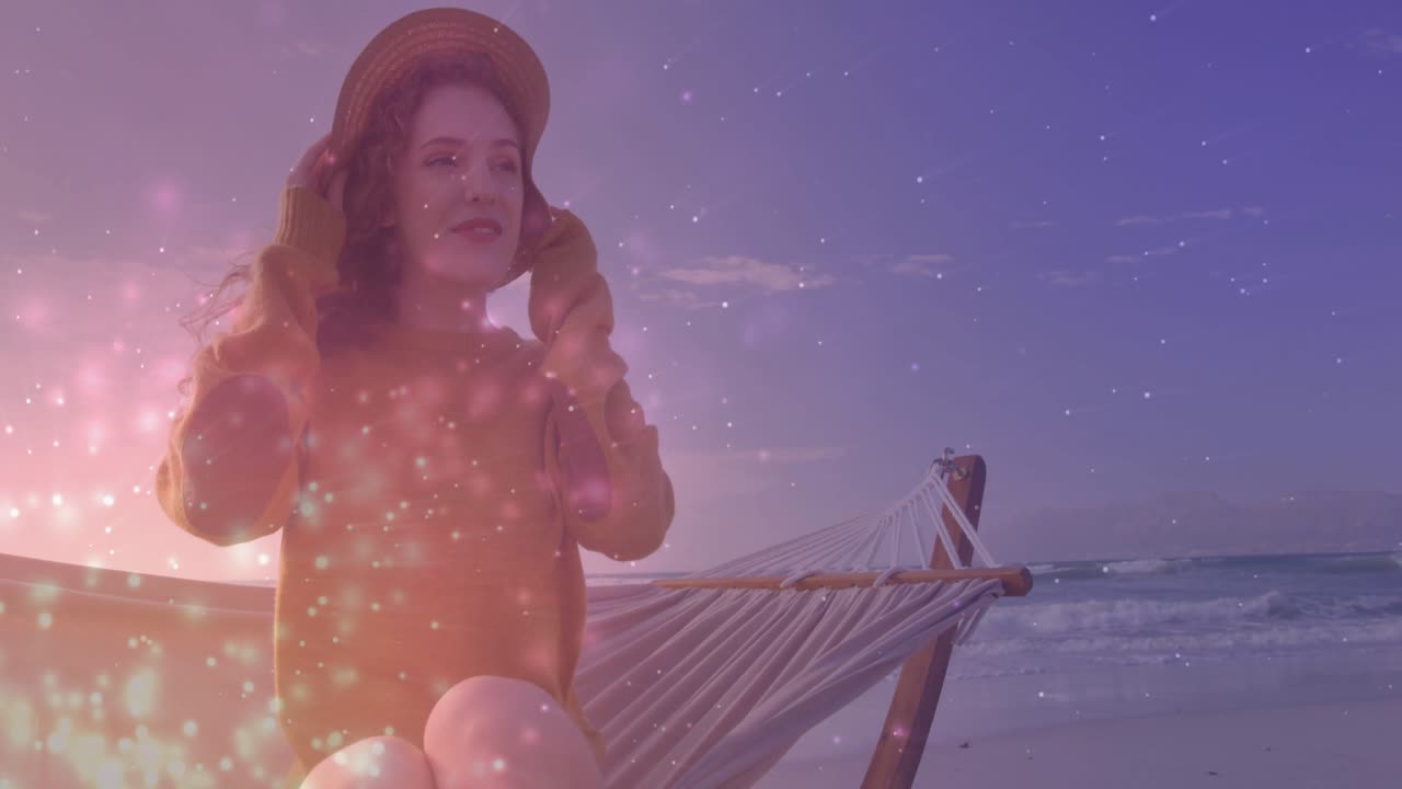 Donna in amaca che solleva un cappello di paglia contro la brezza, con una sovrapposizione scintillante che aggiunge un'atmosfera da spiaggia per lo stile di vita