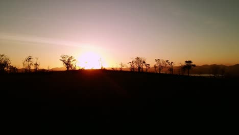 aerial drone shot of dramatic sunset, flying above silhouette of trees and hills