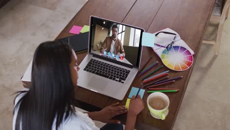 Caucasian-woman-using-laptop-on-video-call-with-male-colleague-and-making-notes-working-from-home