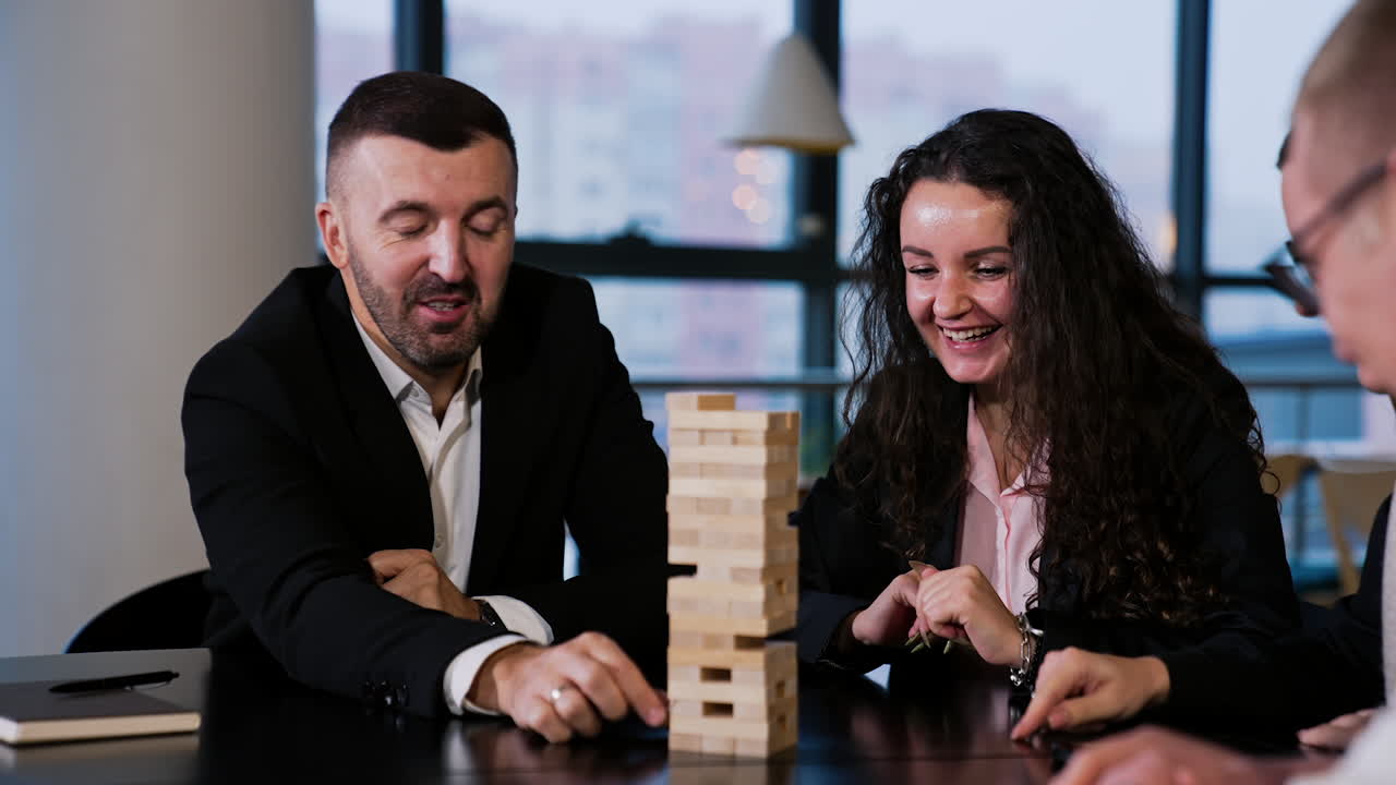 Adult people having fun playing table game. Smiling players take turns pulling carefully little wooden bricks from a pile.