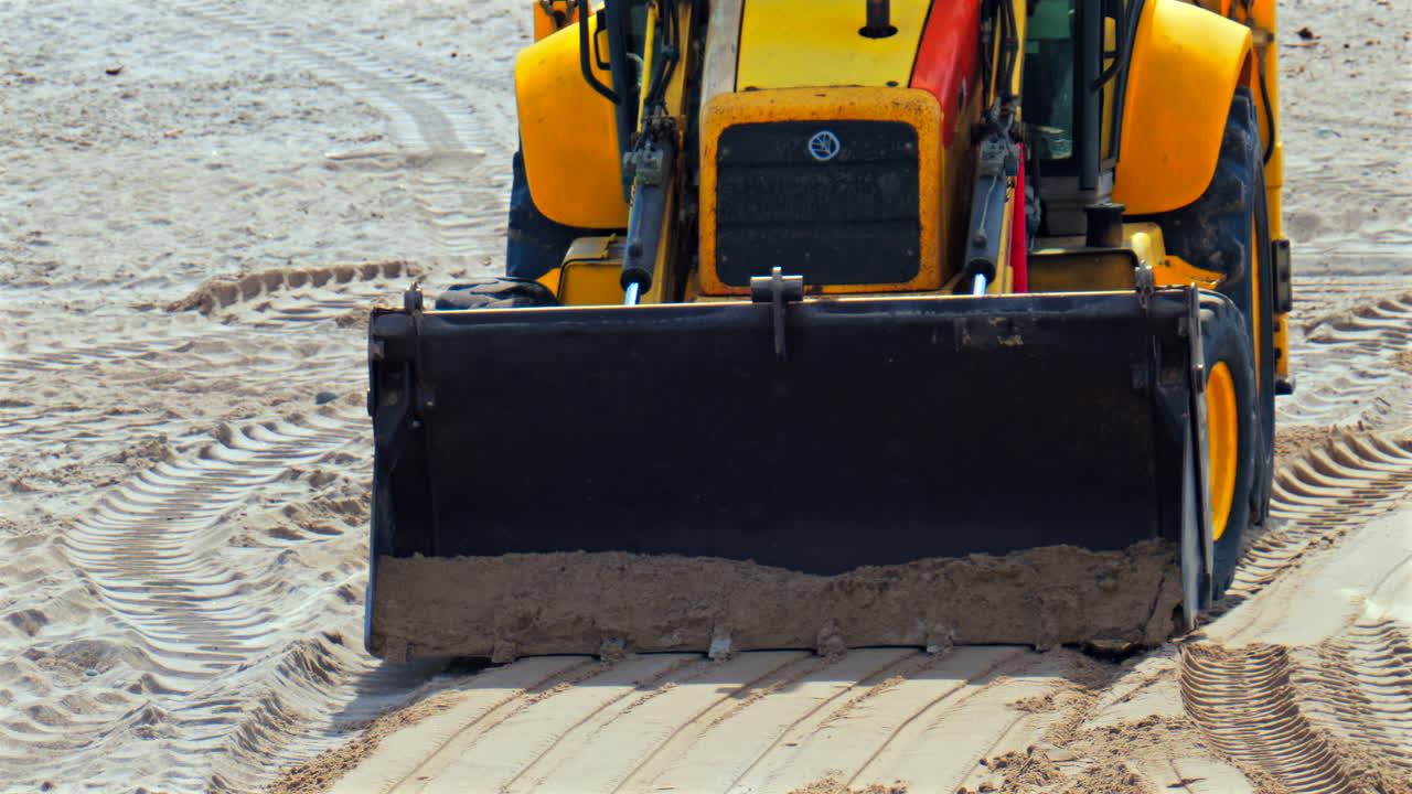 Close up of an yellow wheel loader moving on the sandy beach