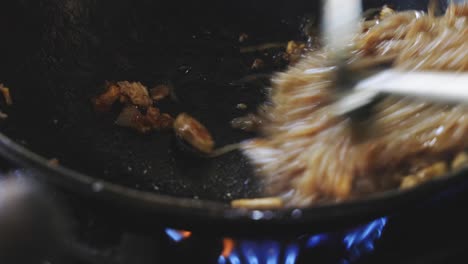 cooking pad thai series: chef quickly stir-frying rice noodles with pad thai sauce and other ingredients in smoking hot pan at thai street food restaurant