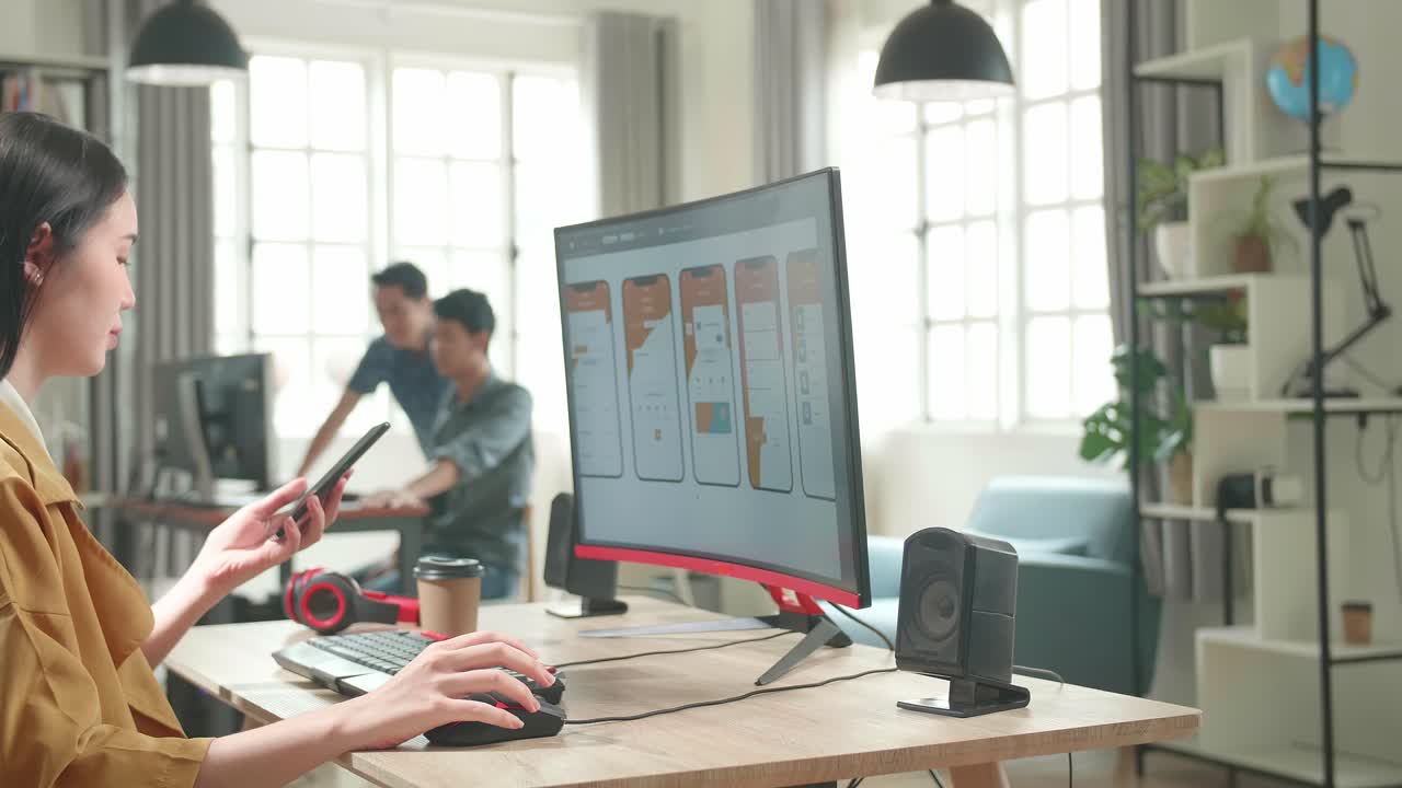 Asian Female Mobile Application Developer Works And Talking On Mobile Phone With Graphics On Her Personal Computer In Office