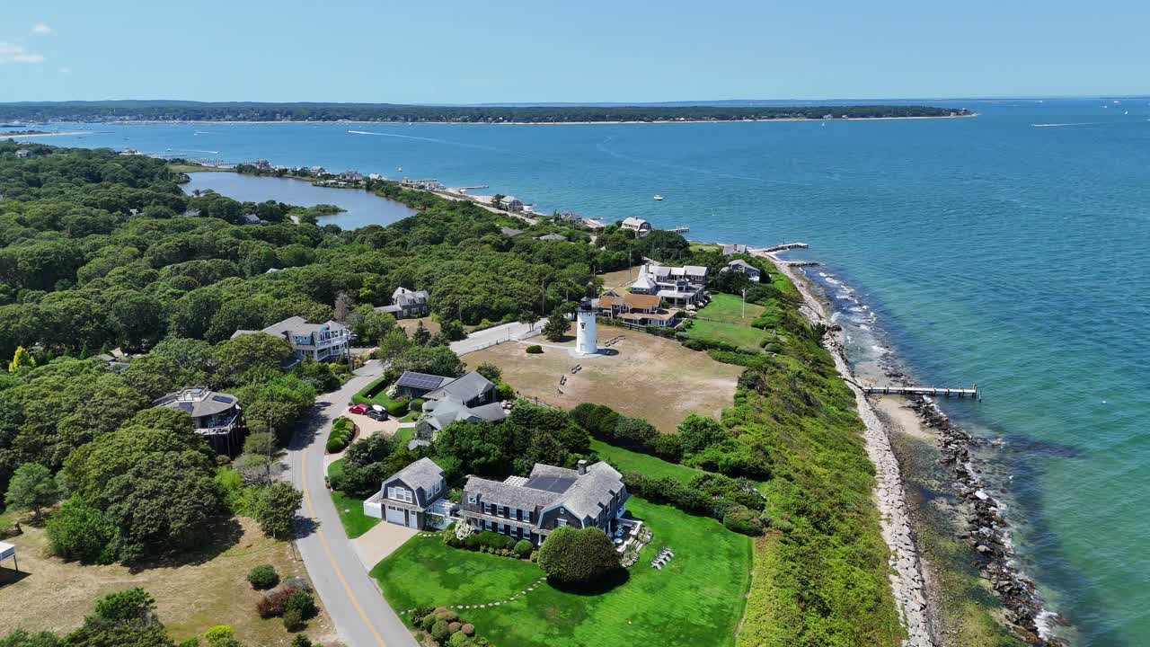 Vista aerea con drone di un faro a Martha's Vineyard, Massachusetts, che si affaccia sulla costa atlantica con acqua turchese, case costiere e vegetazione lussureggiante su un paesaggio insulare estivo e panoramico.