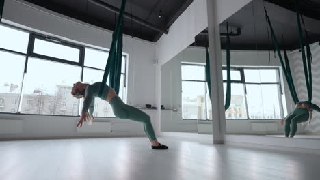 young beautiful woman practice in aero stretching swing. young woman rolls her head upside down in a hammock for aerial yoga. focused pretty mature woman doing aerial yoga in gym