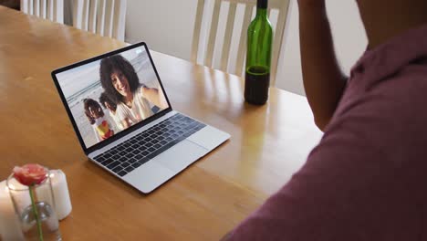 Mid-section-of-african-american-man-drinking-wine-while-having-a-video-call-on-laptop-at-home