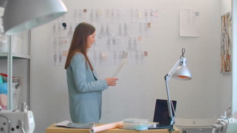 joven diseñador de moda de pie con la espalda a la cámara mirando dibujos bocetos colgados en la pared. la mujer está pensando en una nueva colección de ropa de moda