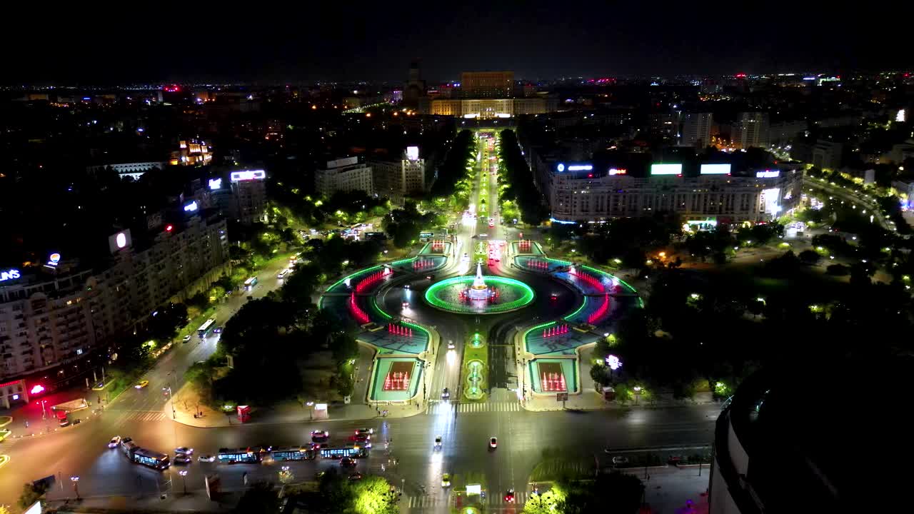 Aerial drone perspective of Union Square, Bucharest city, at night. Famous colored artesian fountains. Drone going backwards above the main boulevard. City traffic at night.