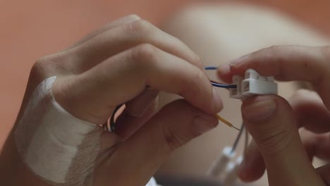 Close-up-to-bandaged-hand-using-self-locking-electrical-cable-connectors-to-connect-wires