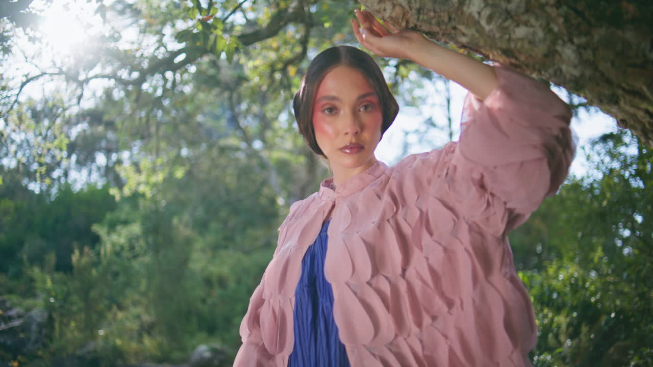 동화 속의 숲을 포즈로 하고 나무 줄기에 기대어 가까이 쳐다보며 매료시키는 여자