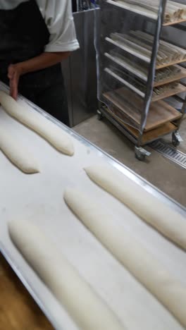 panadero arreglando la masa de baguette en una hoja de hornear
