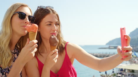 dos mujeres disfrutando de helado y tomando una selfie junto al mar