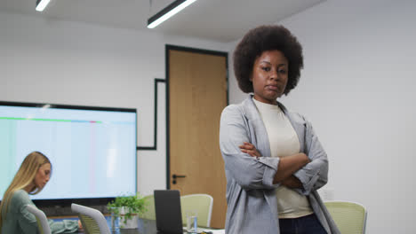 Portrait-of-african-american-businesswoman-smiling-in-office,-with-colleague-working-in-background