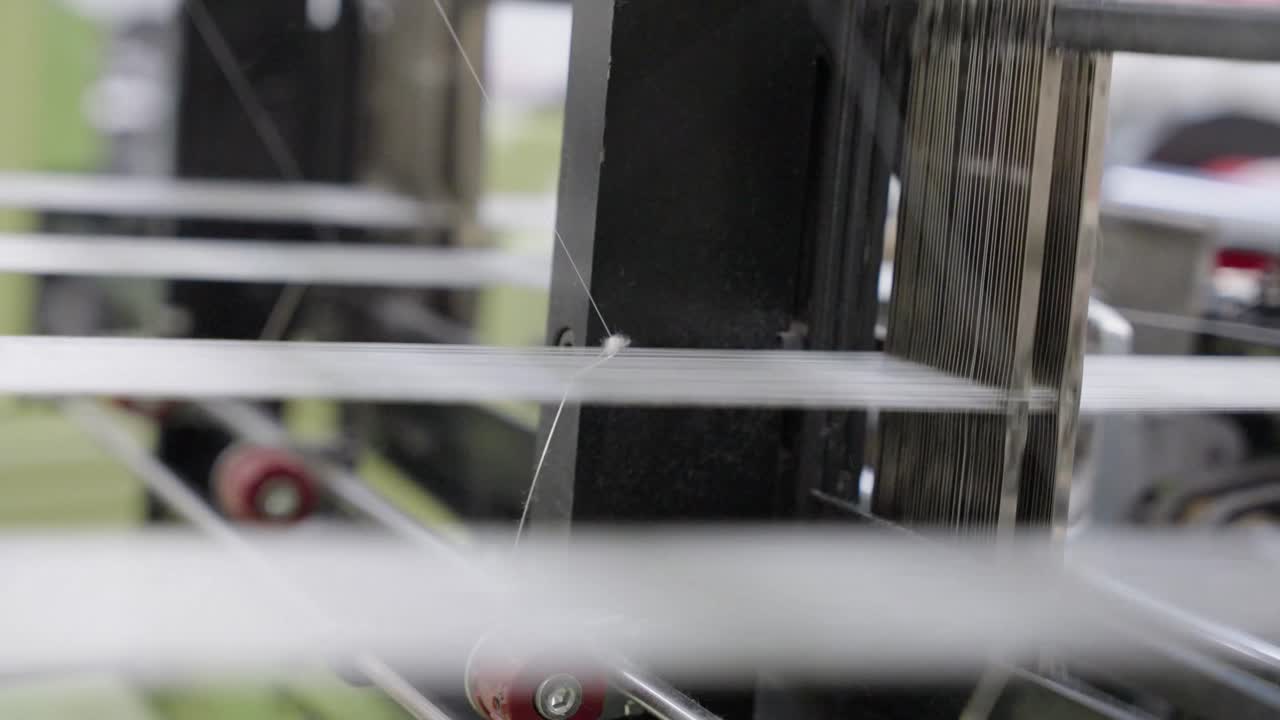 Close-up de uma máquina de tear em funcionamento, exibindo fios, peças móveis e o processo de tecelagem, ideal para fabricação têxtil, artesanato, produção industrial e visuais de máquinas.