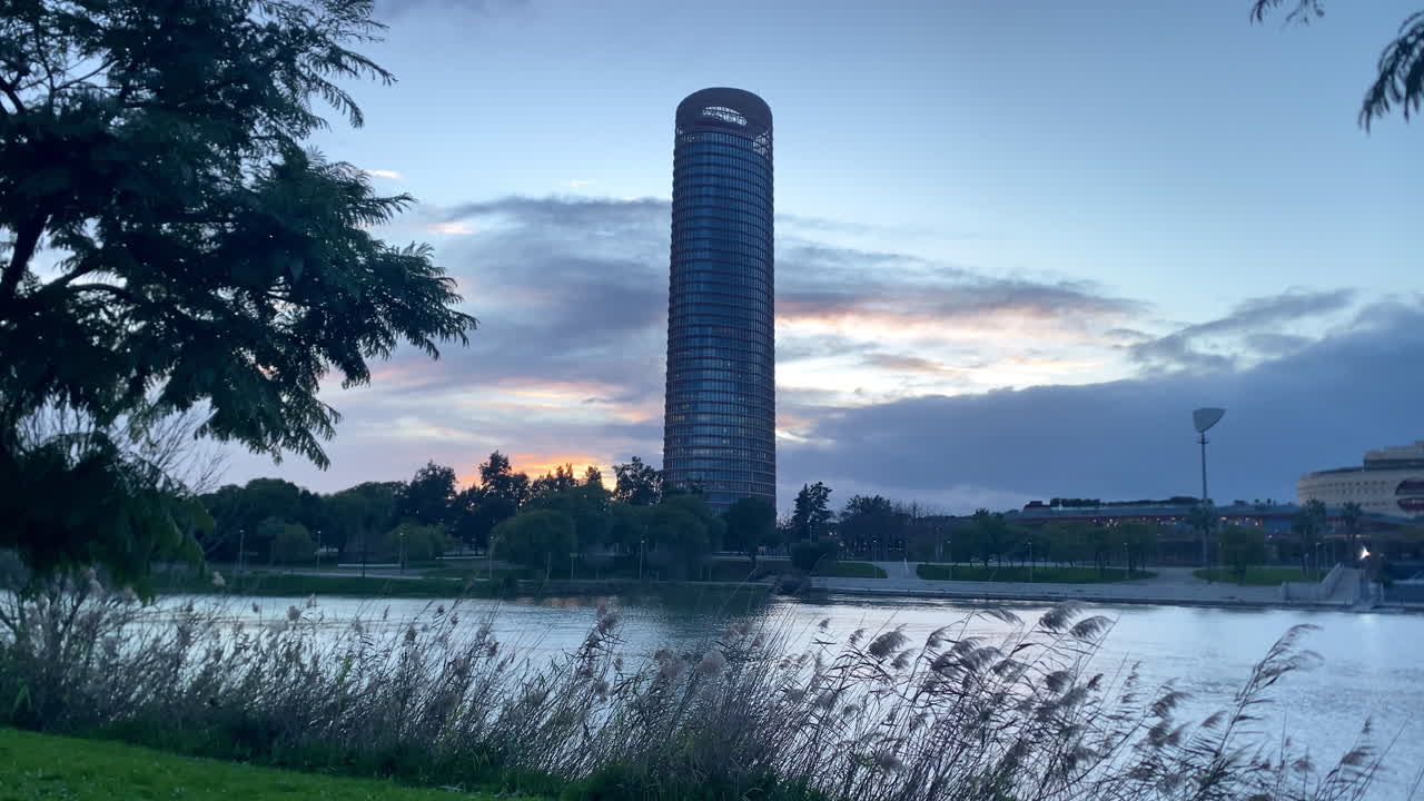 Rascacielos Torre Sevilla erguido junto al río Guadalquivir, con un paisaje urbano y un cielo resplandeciente al atardecer