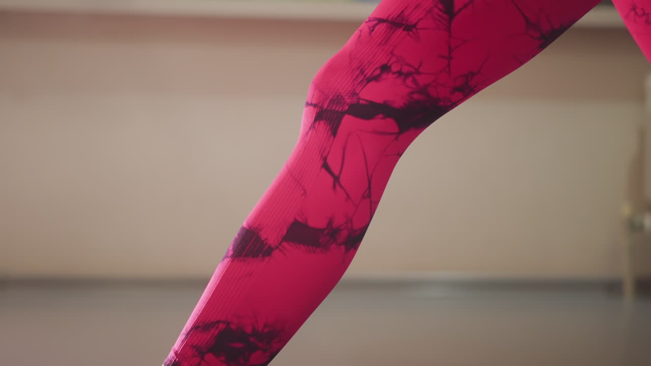 woman on mat in pink leggings performing ankle stretch with wool socks, focused balance and controlled breathing, morning home studio light, slow mobility routine for flexibility and joint care