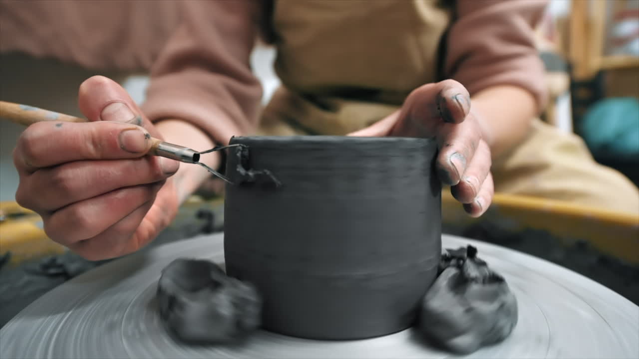 The master of sculpting pottery working in a studio. Shaping the clay on the potter's wheel using a tool. Slow motion