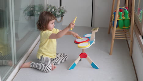 cute blonde baby girl playing toy drums at home