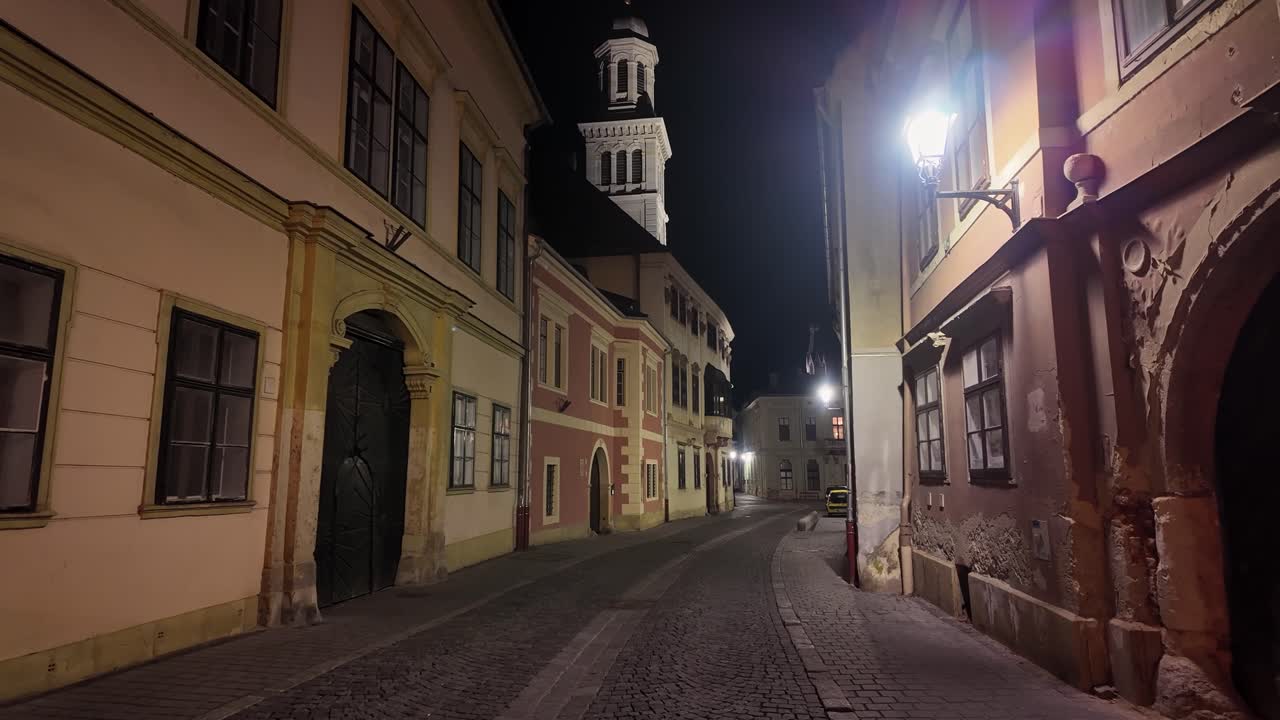 A calm night walk through the streets of town center of Sopron, Hungary, showcasing the historic architecture and beautifully illuminated buildings.