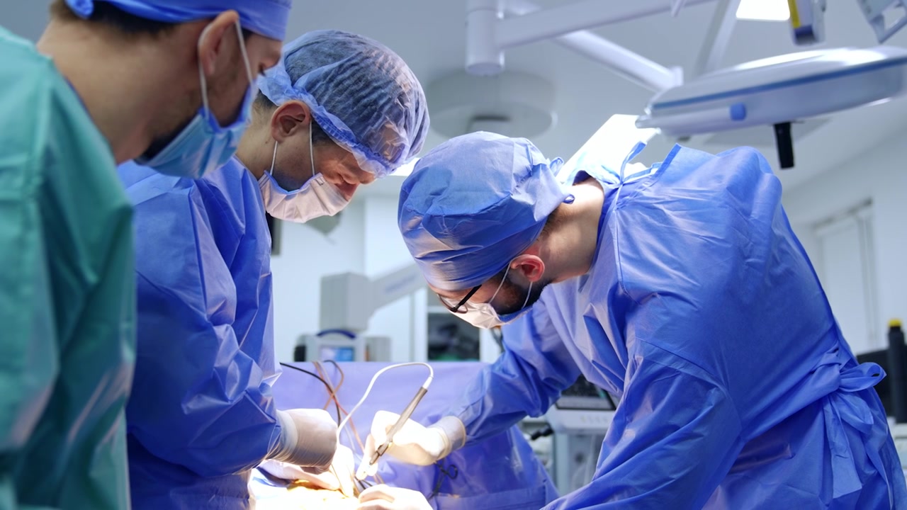 Squadra di chirurghi che collaborano durante un'operazione. Il chirurgo capo si china sul paziente e applica uno strumento.
