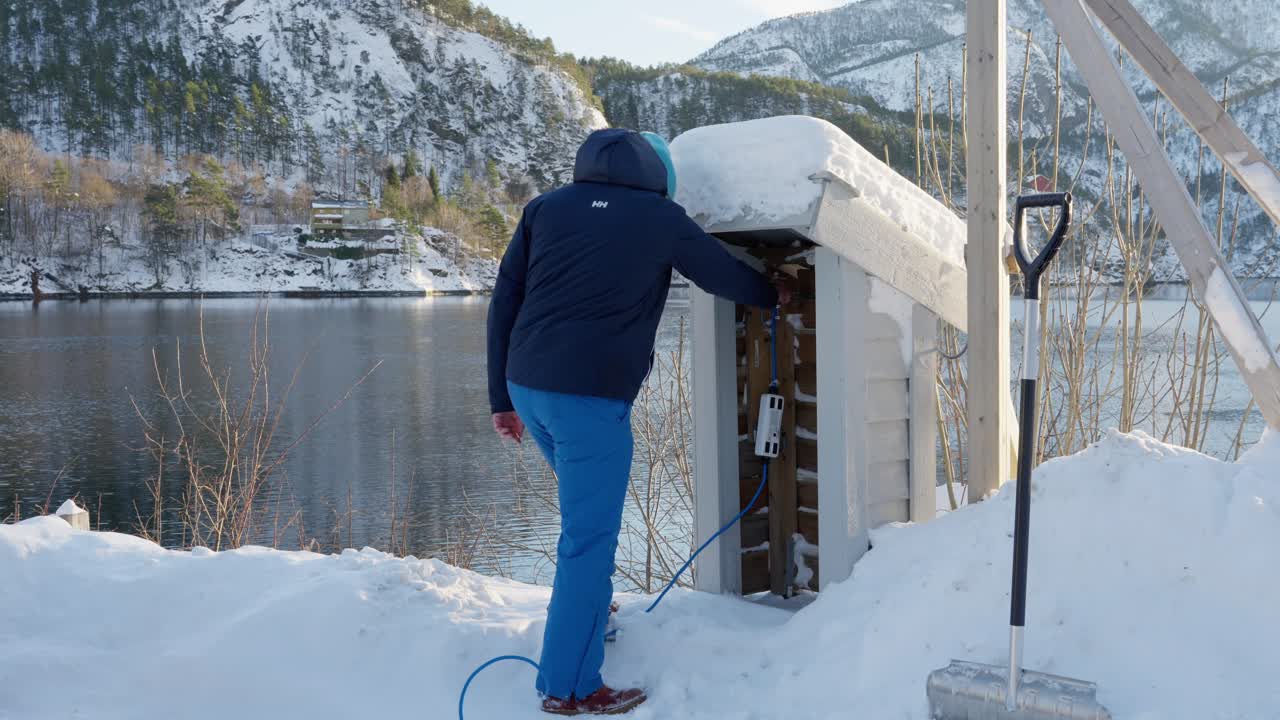 Man unplugs charging brick, cord for his electric car from small hut on winter morning in Norway.