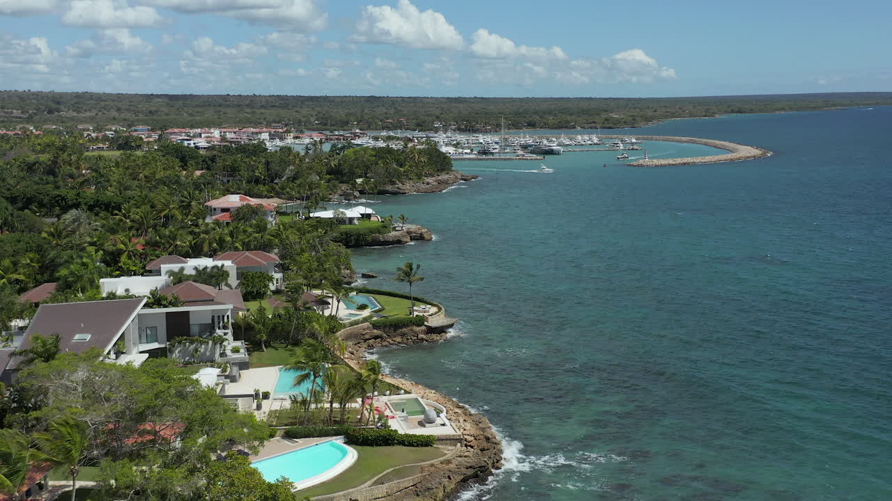 Aerial forward flight over the coastline viewing resort luxury villas, a yacht navigating out of a marina in La Romana, Dominican Republic