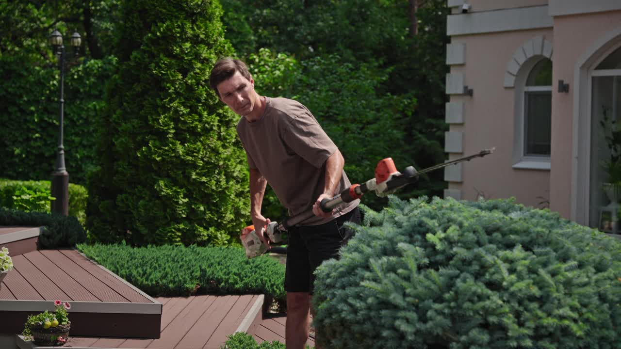 Man Trimming a Bush with a Hedge Trimmer in a Garden