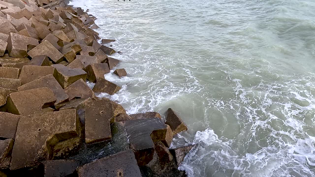 Bølger rammer betonblokke ved kysten.