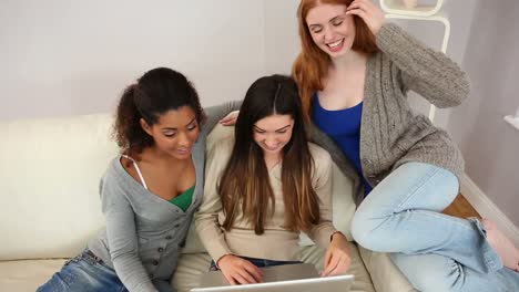 mujeres jóvenes divertidas usando un cuaderno sentadas en el sofá