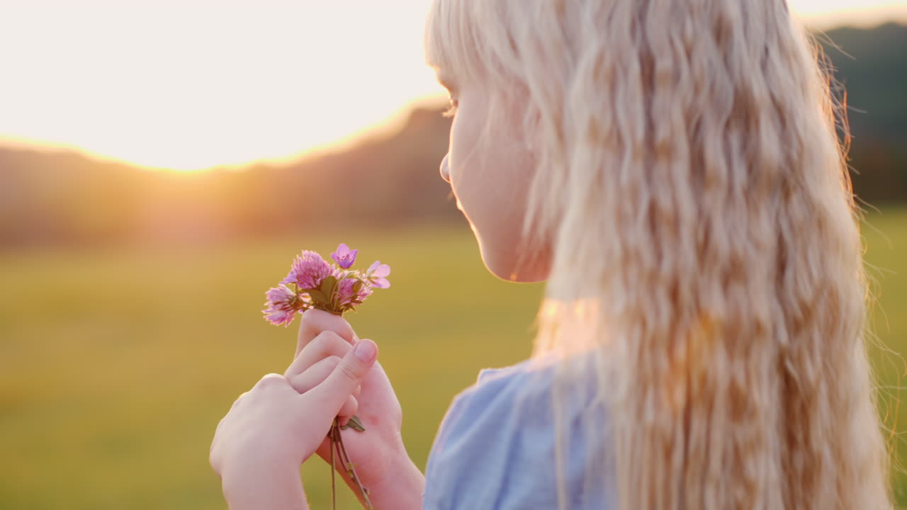 chica rubia de 6 años con un ramo de flores silvestres de pie en el campo al atardecer vista lateral lenta