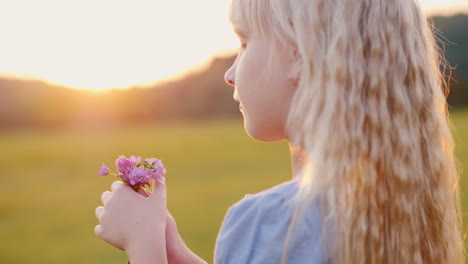 blonde girl 6 years old with a bouquet of wildflowers standing in the field at sunset side view slow