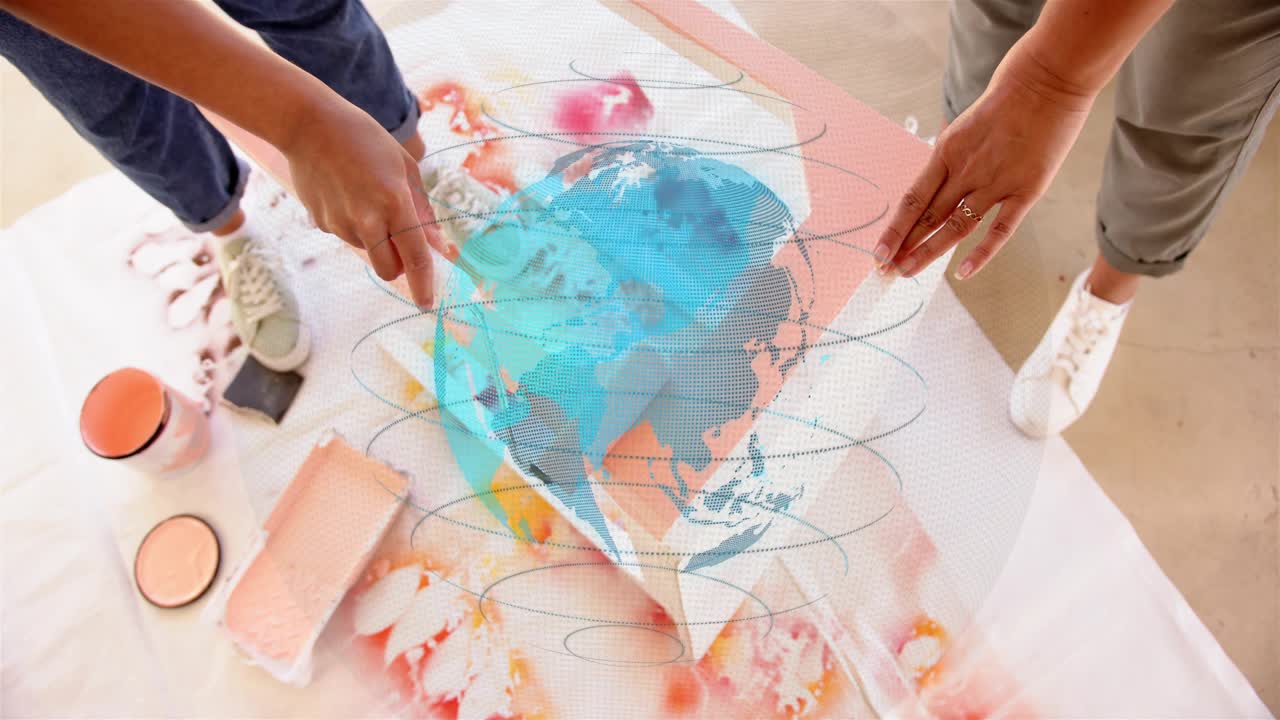 Woman dipping roller and rolling paint for craft panel as partner holding panel blue globe shifting