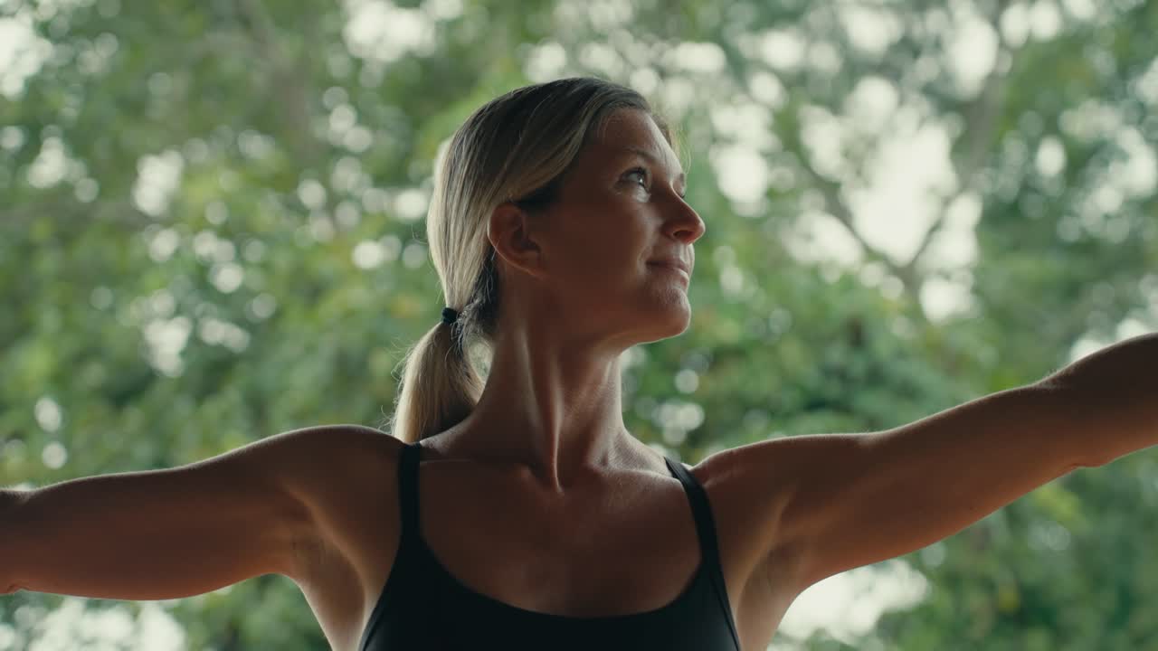 Donna bionda caucasica, in forma e felice, esegue la posizione yoga del guerriero con fumo che passa e vegetazione verde lussureggiante sullo sfondo, primo piano