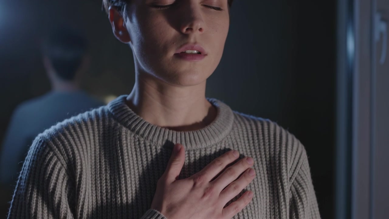 Una donna che respira posiziona la mano destra sullo sterno e si centra allo specchio, con un maglione a coste.