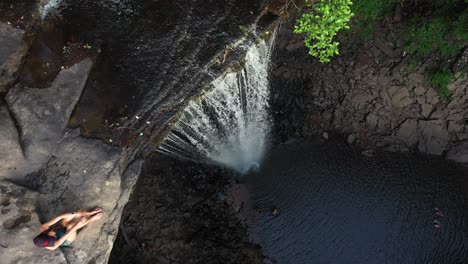 vista aérea de ángulo alto de una mujer sentada en un acantilado y en la parte superior de una cascada escénica en el campo de tennessee, ee.uu.