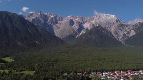 drone flying sideways to the right along a massive alp mountain side view with woods and houses in europe