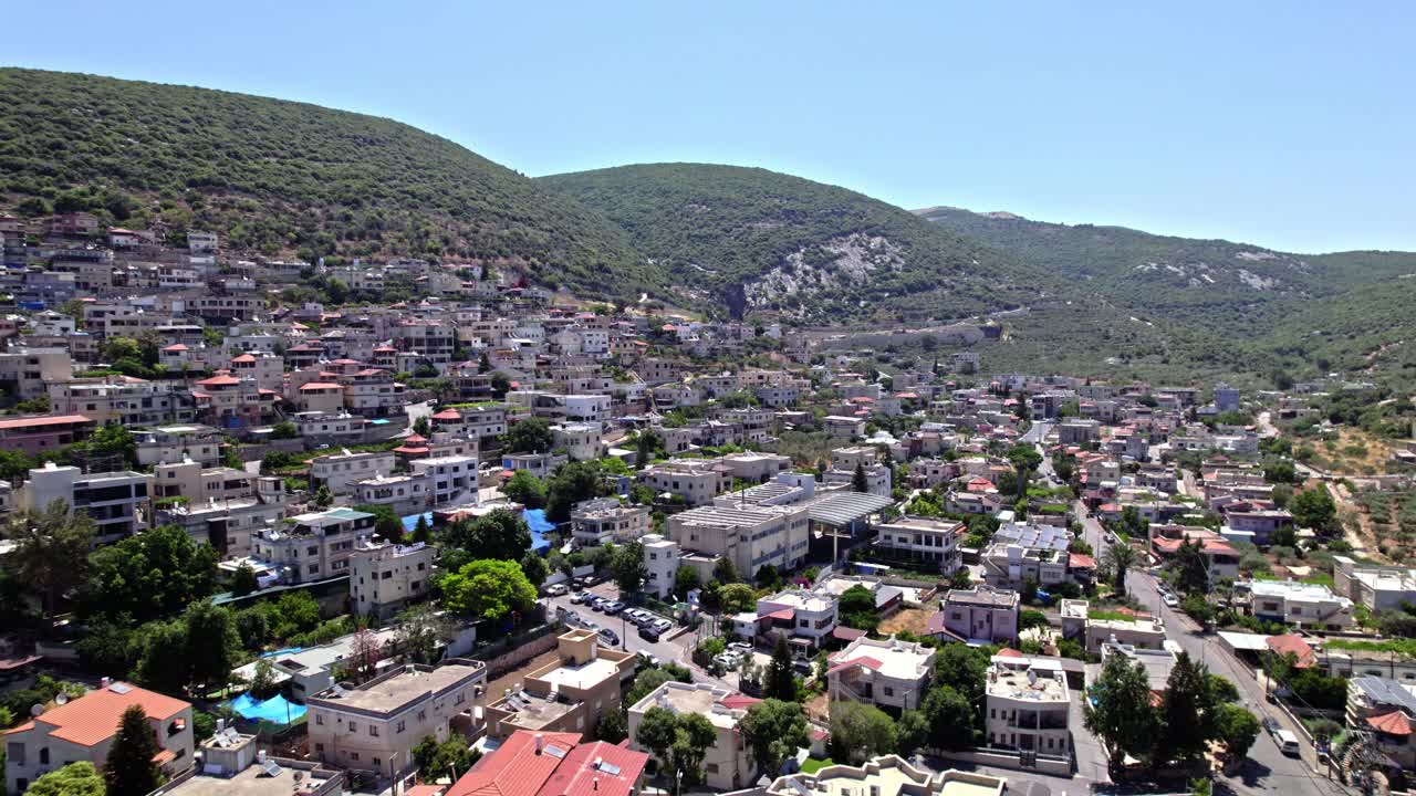 Aerial view of the Druze town of Peki'in in northern Israel, surrounded by lush green mountains under a clear summer sky.
