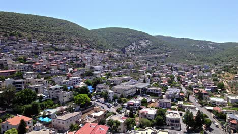 aerial view of the druze town of peki'in in northern israel, surrounded by lush green mountains under a clear summer sky.