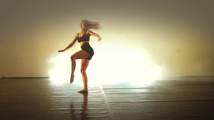 Pretty young actress performing gentle dance elements of modern contemporary choreography in smoky backlit studio